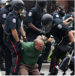 John Pruyn, being dragged way by riot police after having his artifical leg removed. The Welland Ontario federal government worker and part-time farmer was locked in a makeshift jail, then released without any charges or explanation for his detention, a day later. He had been sitting on the grass near Queen's Park in Toronto, listening to citizen activists offer talks on jobs, environmental protection and other issues before being dragged away.